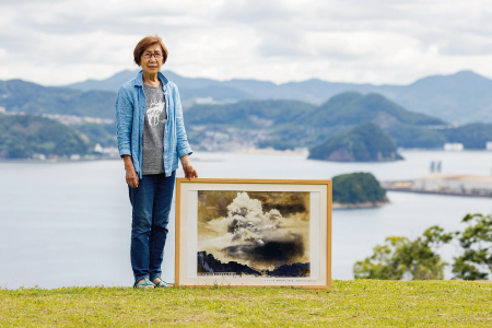 原爆投下直後の旧香焼村を撮影した写真と津村はるみさん。背後が爆心地（長崎市香焼町）